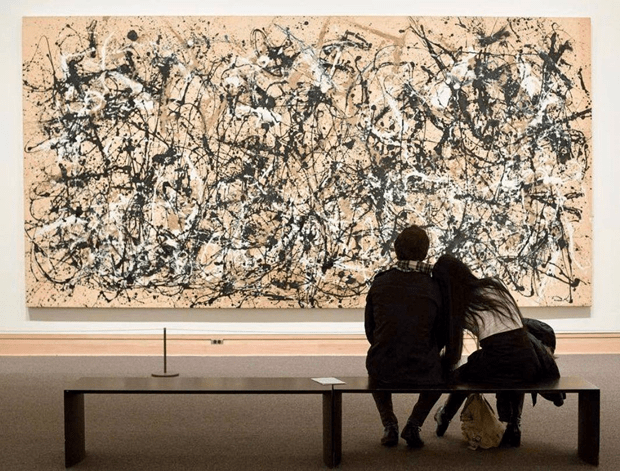 A man and a woman sitting and looking at a painting.